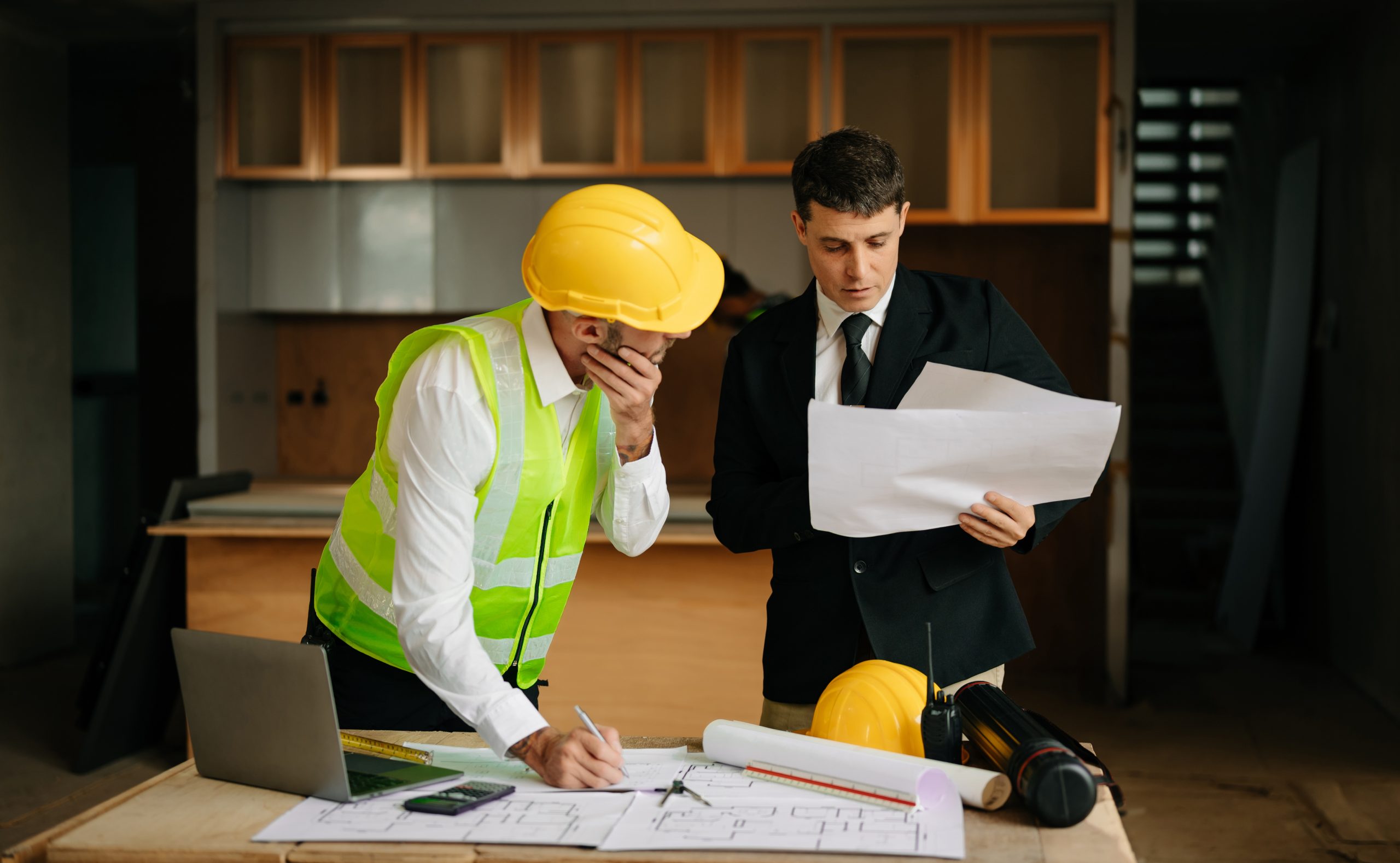 Contractor and architect looking at plan, tablet, laptop and tal