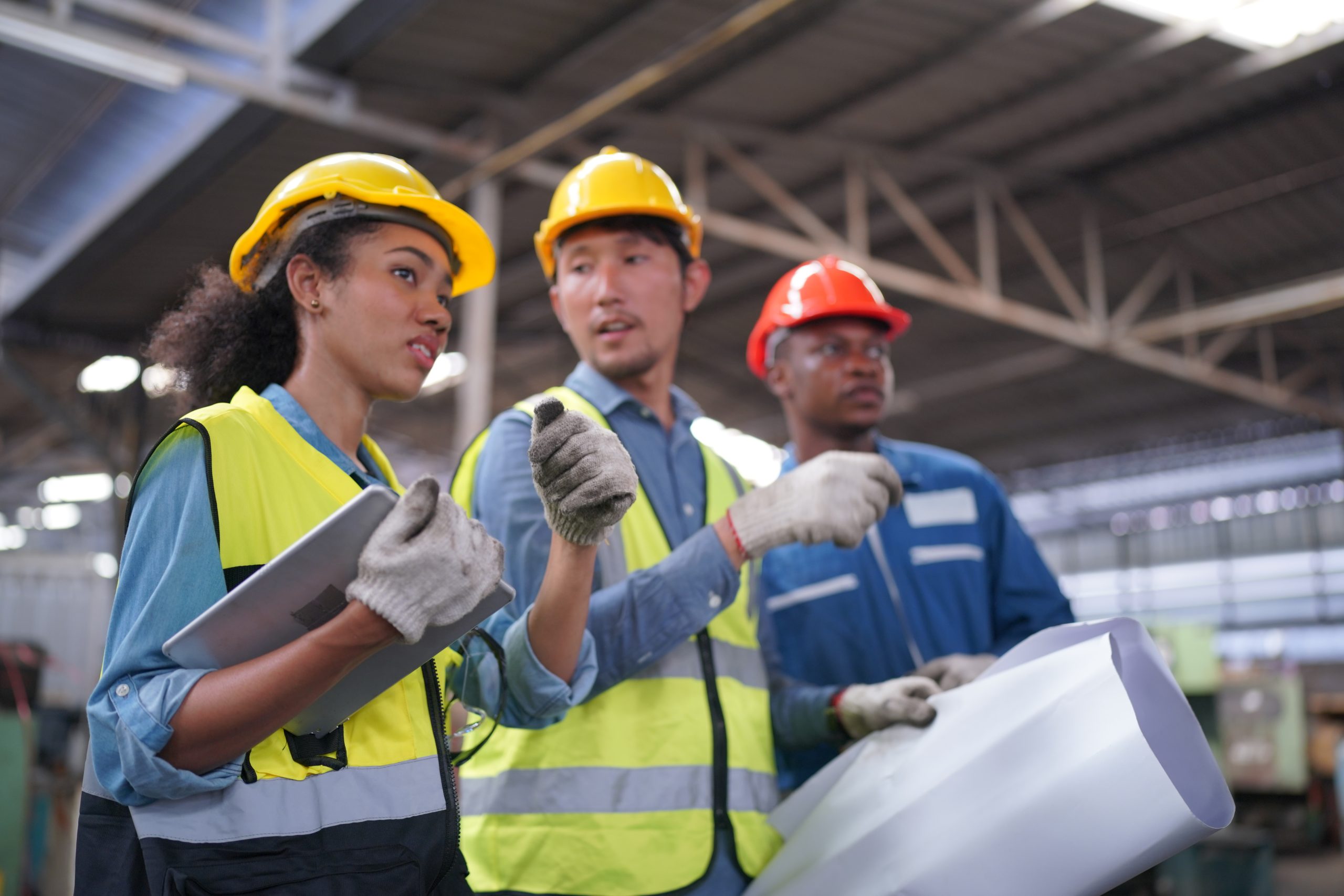 Male and Female Industrial Engineers Talk with Factory Worker against machines and equipments background. They Work at the Heavy Industry Manufacturing Facility.